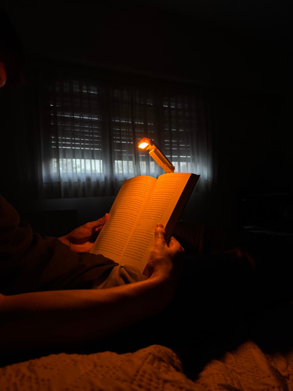 LUMIA enganchada a un libro, iluminando solo la página durante una lectura nocturna en la cama